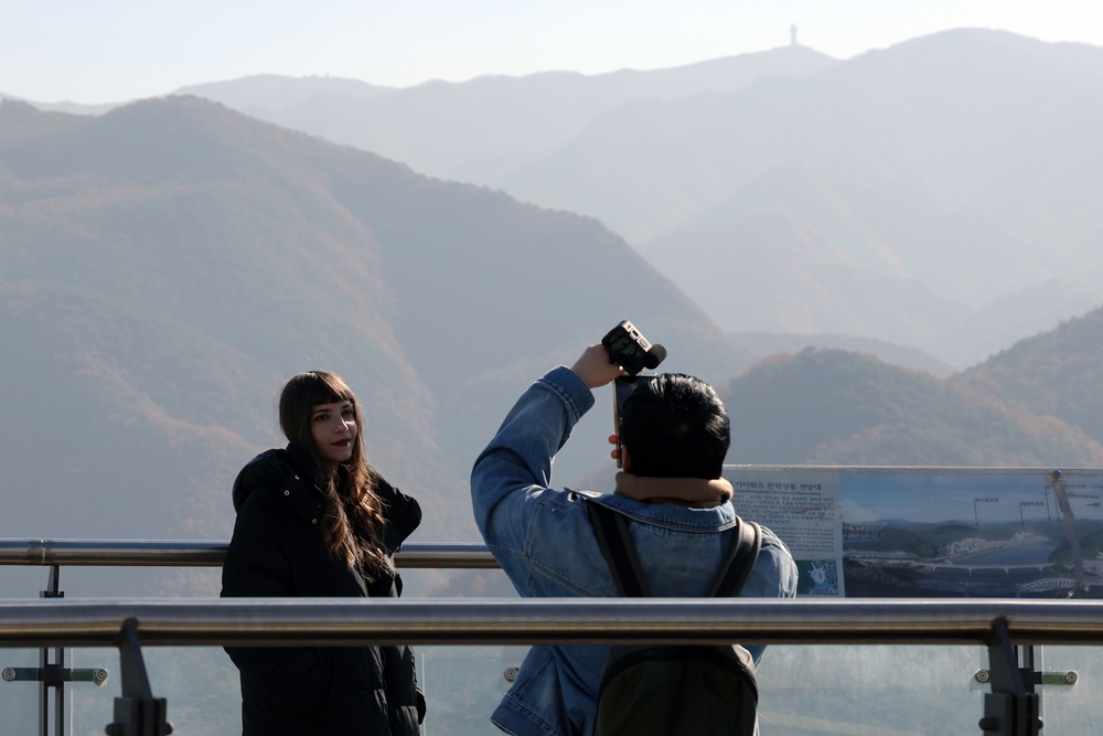 Thai K-influencer Aiyaphat Wankawisant on Nov. 6 takes a photo of Honorary Reporter from Greece Foteini Chatzoudi at the top of Mancheonha Skywalk in Danyang-gun County, Chungcheongbuk-do Province, with a view of mountains in the background.